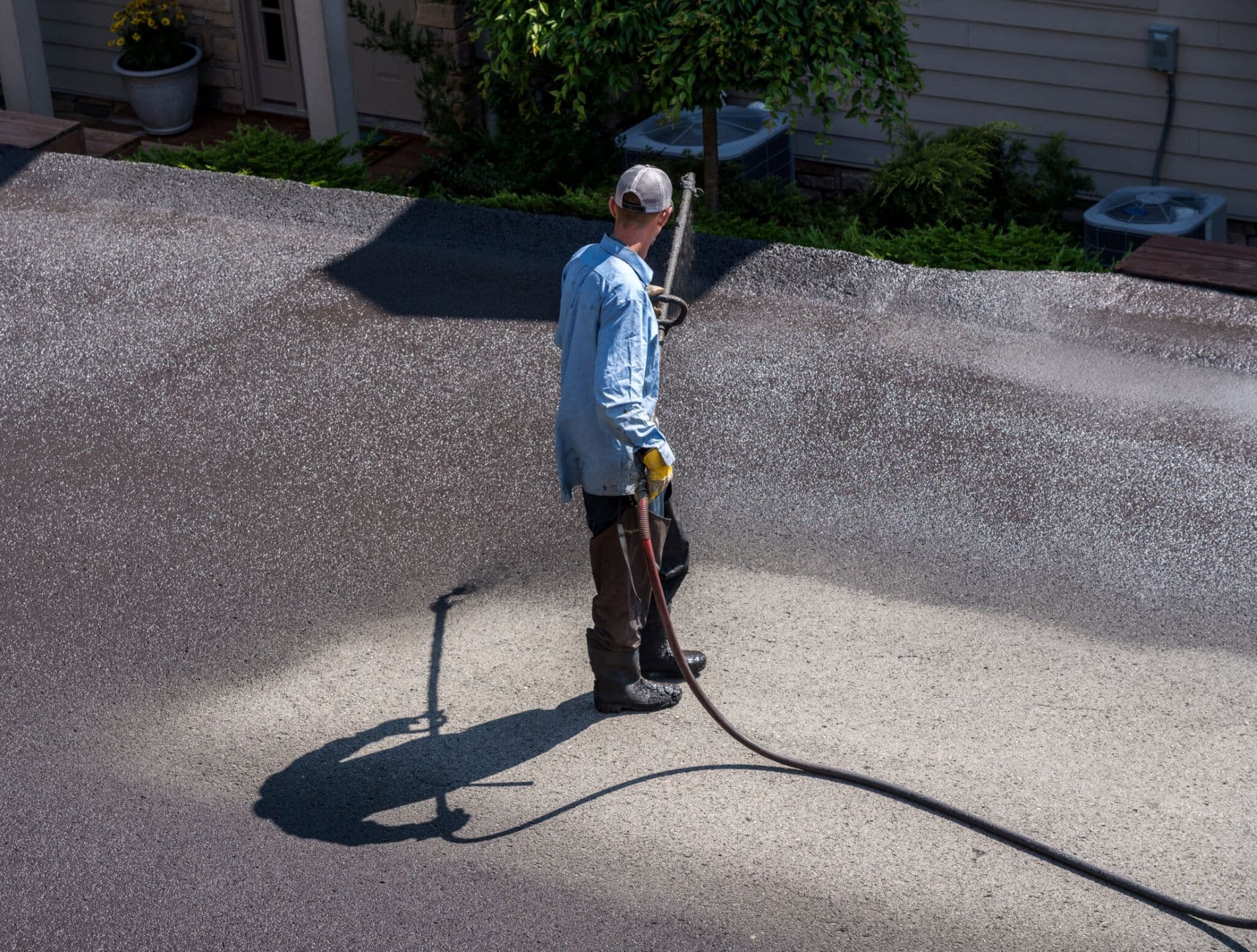 Worker spraying sealcoating onto asphalt